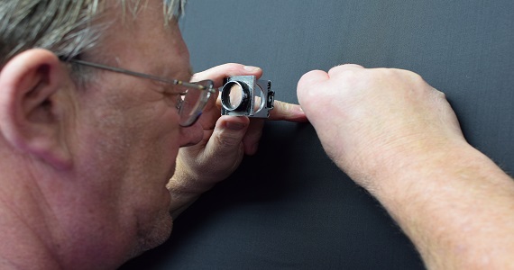 man inspecting a blue fabric with a magnifying glass.